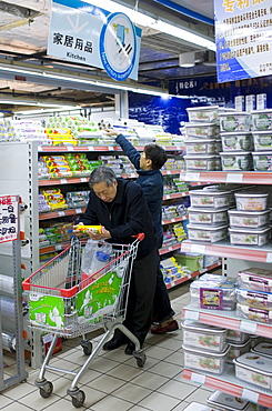 Man with shopping trolley reading product details while buying in supermarket in Chongqing, China