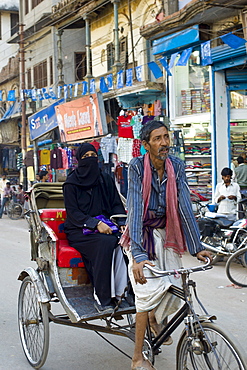 Street scene in holy city of Varanasi, young muslim woman in black burkha rides in rickshaw, Benares, Northern India