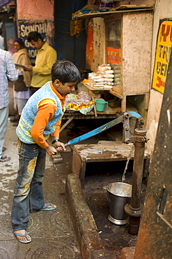 Indian boy using water pump in alleyway in the holy city of Varanasi, Benares, Northern India