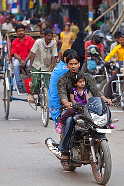 Fathers with children on cycles in crowded street scene during holy Festival of Shivaratri in city of Varanasi, Benares, Northern India