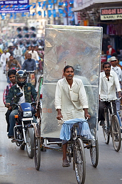 Indian man driving rickshaw with heavy load in street scene in city of Varanasi, Benares, Northern India