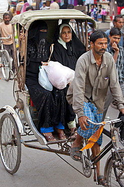 Muslim women travel by rickshaw in crowded street scene in city of Varanasi, Benares, Northern India