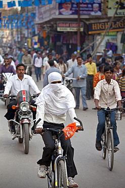 Muslim woman with hijab burkha veil covering head and face cycles in the street in city of Varanasi, Benares, Northern India