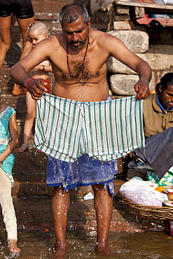 Indian Hindu pilgrim bathing and washing his clothes in The Ganges River at Dashashwamedh Ghat in Varanasi, India