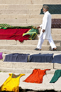 Indian man walks past laundry drying on the steps of Kali Ghat by the The Ganges River in City of Varanasi, Benares, India