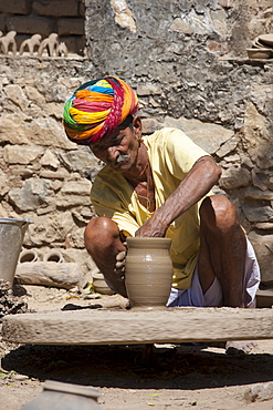 Indian potter in traditional Rajasthani turban works on potter's wheel at home making clay pots in Nimaj village, Rajasthan, Northern India