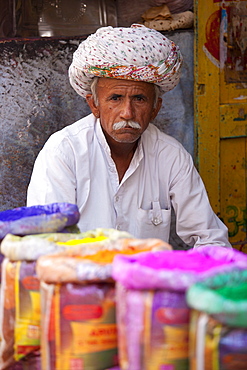 Indian man selling powder paint colours for Holi festival on sale at Katala Bazar in Jodhpur, Rajasthan, Northern India