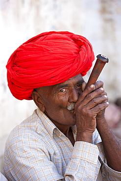 Indian man wearing Rajasthani turban smokes traditional clay pipe in Narlai village in Rajasthan, Northern India