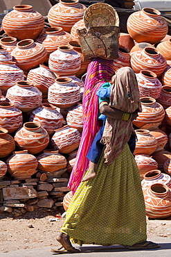 Indian woman out shopping carrying child walks past clay water pots on sale in old town Udaipur, Rajasthan, Western India,