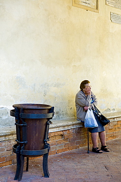 Elderly lady stops for a rest by Piazza Pio II after shopping in the market in Pienza, Tuscany, Italy