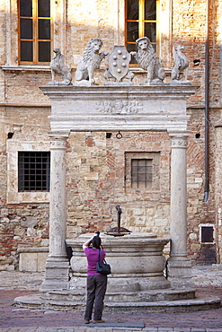 Tourist photographs well of griffins and lions by Palazzo del Capitano del Popolo in Piazza Grande, Montepulciano, Tuscany, Italy