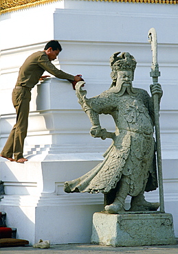 A worker cleaning at the Grand Palace in Bangkok, Thailand. In front an impressive statue stands guard.