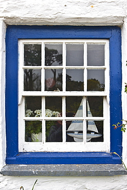 Sailing yacht and vase of flowers in bright blue window of Rose Cottage at Helston in Cornwall, UK