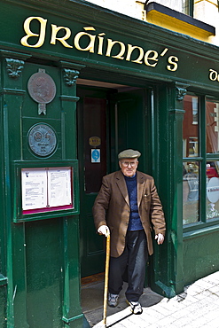 Elderly local Irishman with walking stick leaving Grainne's Bar in Mill Street, Timoleague, West Cork, Ireland