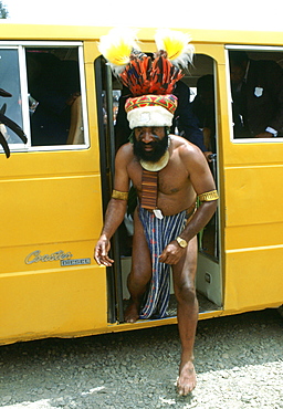 Bearded tribesman in feathered headdress steps from a modern minibus during  a gathering of tribes at Mount Hagen in Papua New Guinea