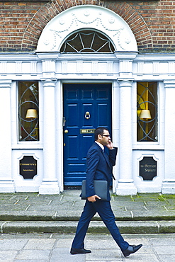 Businessman using cellphone passes traditional doorway with fanlight windows in Merrion Square, Dublin, Ireland