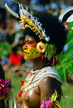 Bare-breasted native woman wearing a feathered headdress, beaded necklaces and face paints during  a gathering of tribes at Mount Hagen in Papua New Guinea