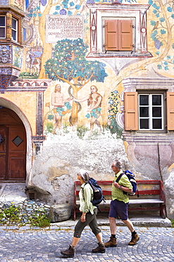 Tourists pass Adam and Eve mural and Romansch inscription painted on 17th century houses, village of Ardez, Engadine Valley, Graubunden, Switzerland, Europe