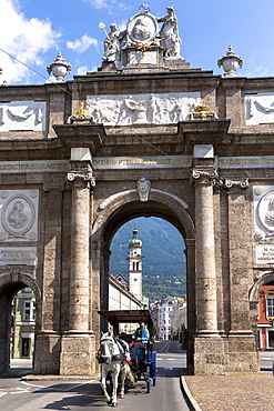 Tourists in horse-drawn carriage pass Triumphal Arch and Spitalskirche in Innsbruck, the Tyrol, Austria, Europe