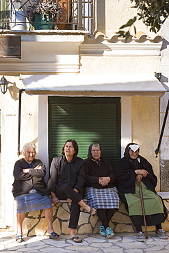 Elderly Corfiot women wearing traditional black clothes sitting relaxing in village square of Krini, Corfu, Greek Islands, Greece, Europe