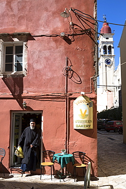 Greek Orthodox priest in traditional robes buying bread from bakery shop in Kerkyra, Corfu Town, Corfu, Greek Islands, Greece, Europe