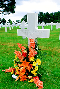 Headstones at a United States Military Cemetery at Utah Beach in Normandy, France.  Flowers have been left beside one of the crosses dedicated to a US serviceman.