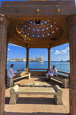 Seated Omani men wearing traditional dishdasha on Mutrah Corniche, with view to Al Said Royal Yacht, Muscat, Oman, Middle East