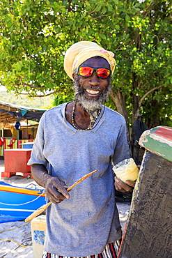 Grinning man repairs boat, colourful Saltwhistle Bay, Mayreau, Grenadines, St. Vincent and The Grenadines, Windward Islands, West Indies, Caribbean, Central America