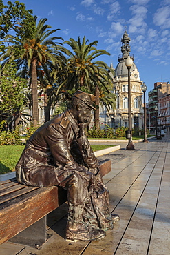 Bronze statue of a sailor on a wooden bench with palm trees, Town Hall backdrop, Cartagena, Murcia Region, Spain, Europe