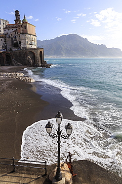 Fancy street lamp, rusty anchor and wave breaking on beach, distant church, Atrani, near Amalfi, Costiera Amalfitana (Amalfi Coast), UNESCO World Heritage Site, Campania, Italy, Europe