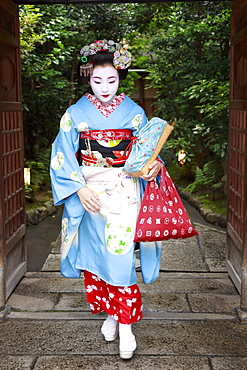 Maiko, apprentice geisha, leaves okiya (geisha house) through garden gate for evening appointment, Gion, Kyoto, Japan, Asia