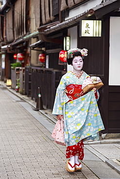 Maiko, apprentice geisha, walks to evening appointment past traditional wooden buildings, Gion, Kyoto, Japan, Asia