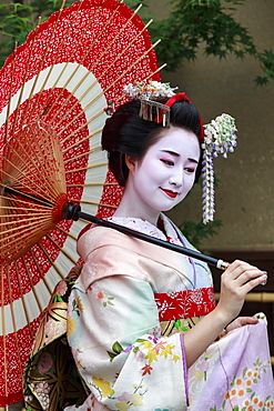 Portrait of smiling geisha in floral robes with red umbrella in summer, Kyoto, Japan, Asia