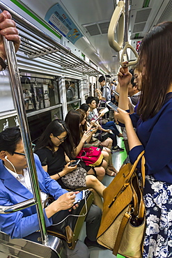 Smartly dressed commuters on the busy subway looking at their phones and e-devices, Seoul, South Korea, Asia