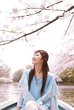 Woman In Rowing Boat On Lake With Cherry Blossom In Background