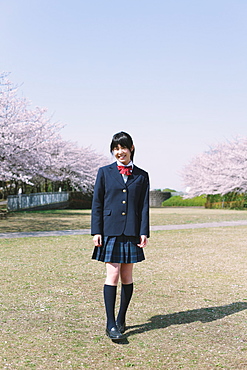 Japanese schoolgirl in her uniform with cherry blossoms in the background