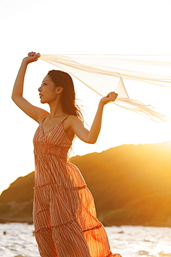 Japanese woman holding a veil in the wind by the beach