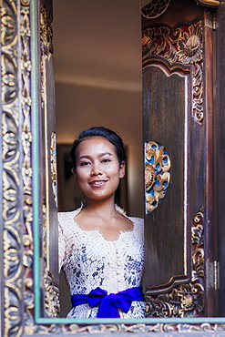 A Balinese woman in traditional dress looking out from a carved window in a local village, Bali, Indonesia, Southeast Asia, Asia