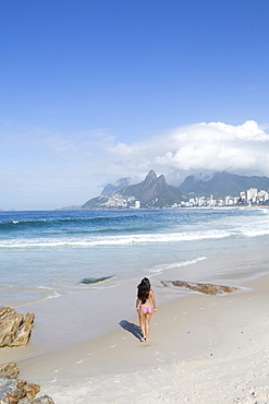 A 20-25 year old young Brazilian woman on Ipanema Beach with the Morro Dois Irmaos hills in the distance, Rio de Janeiro, Brazil, South America