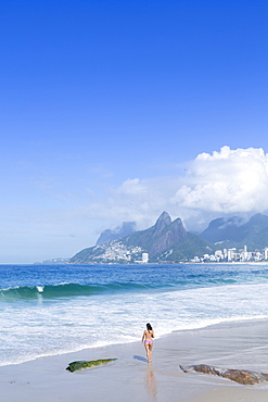 A 20-25 year old young Brazilian woman on Ipanema Beach with the Morro Dois Irmaos hills in the distance, Rio de Janeiro, Brazil, South America