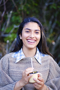 A Patagonian girl in a traditional wool poncho with a bombilla straw drinking yerba mate, Patagonia, Chile, South America