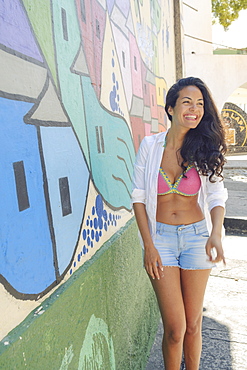 Young Brazilian woman happy and smiling next to a graffiti wall in Lapa, central Rio de Janeiro, Brazil, South America