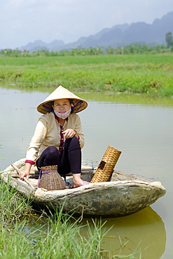 Local village fisherwoman wearing a Non La conical hat and sitting in a concrete lined bamboo boat, Ninh Binh, Vietnam, Indochina, Southeast Asia, Asia