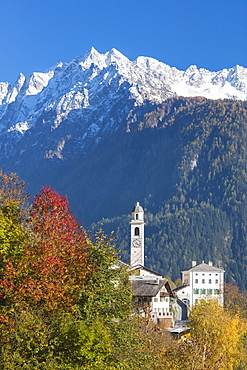 The colorful trees frame the alpine church and the snowy peaks, Soglio, Bregaglia Valley, Canton of Graubunden, Swiss Alps, Switzerland, Europe