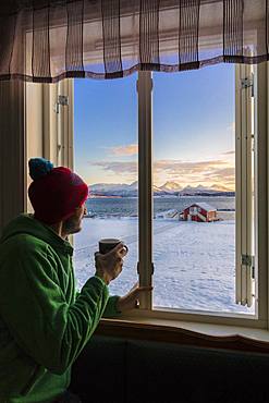 Man looks at the snowy landscape from a window, Troms, Norway, Scandinavia, Europe