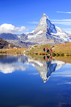 Hikers walking on the path beside the Stellisee with the Matterhorn reflected, Zermatt, Canton of Valais, Pennine Alps, Switzerland, Europe