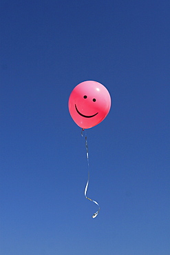 Pink smiley balloon in blue sky, switzerland