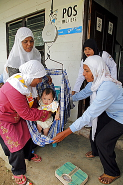 Indonesia growth monitoring (baby weighing) at a posyandu, or mother-child temporary health post in village of paya lumpat. Photograph taken in meulaboh, aceh province -december 2006, 2 years after tsunami of december 26th 2004 devastated much of coastal region. Taken to illustrate reconstruction work projects of (catholic relief services) of sponsored photo tour 