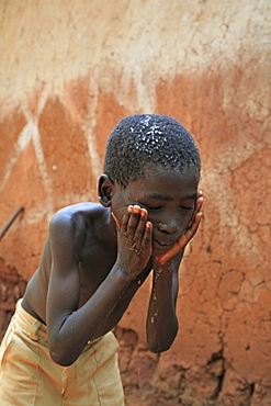 Burundi family of speciose ciza (32) and three children, claude (9), constantin (6) and orave (1). Claude washing his face. Giteraa.