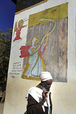 Ethiopia priest walking passed mural depicting abuna aregawi and the serpent, kidana merhet church, tigray